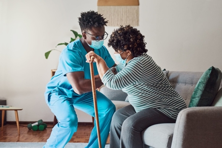 Aide helps a woman with disabilities using a cane off the couch